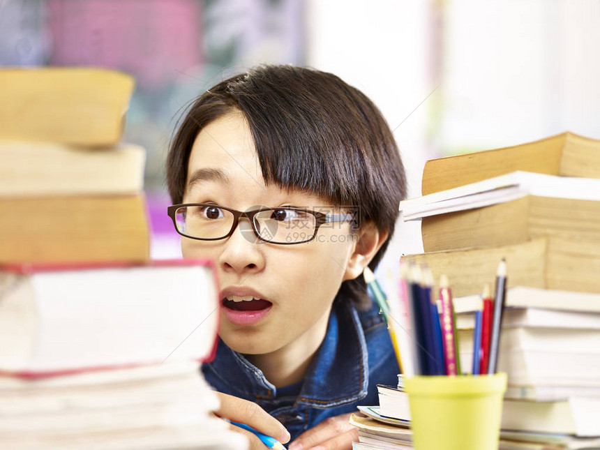 身戴眼镜的亚洲学生似乎对他必须阅读的书籍感到吃惊图片