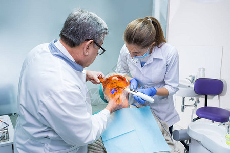 使用紫外线光的牙科医生高级病人和两名牙医图片