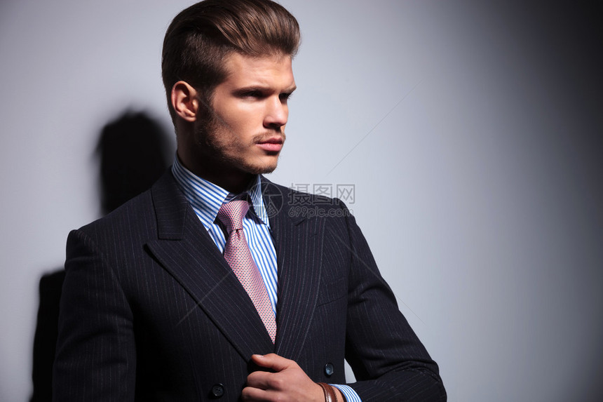 一个穿着经典西装和领带的感年轻男人的侧面将他的项圈放图片