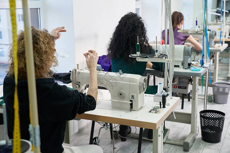 年轻的裁缝女人在缝纫机上缝制衣服微笑的女裁缝和她的手关闭在车间专注于图片