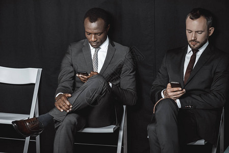 在等待工作面试时使用智能手机穿衣的多文化企业家图片