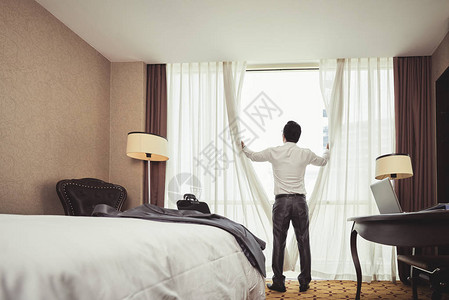 商人在酒店房间拉开窗帘的后视图背景图片