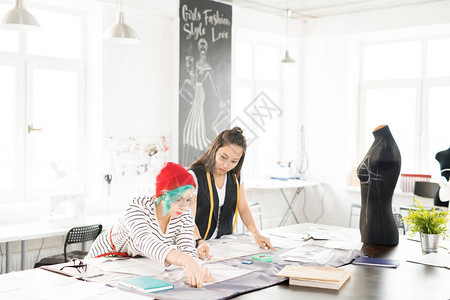 两位当代年轻女在裁缝桌上为定制服装制作图案的广角肖像图片