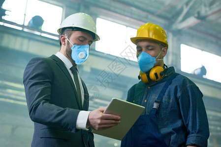 两名工程师戴防护面罩和安全帽在危险工业厂房工作的画图片