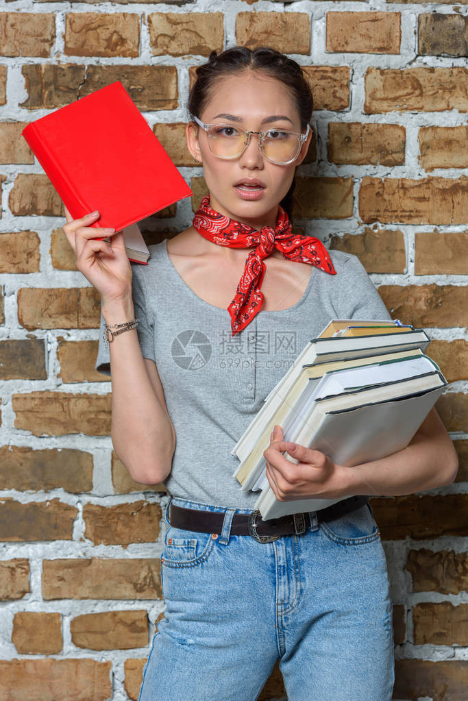 拿着书和看照相机的时髦的亚裔女孩图片