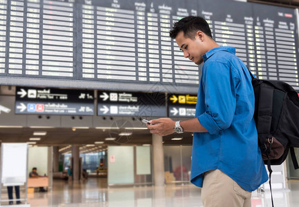 亚洲旅客使用智能手机在现代机场的航班信息屏幕上办理登机手续图片