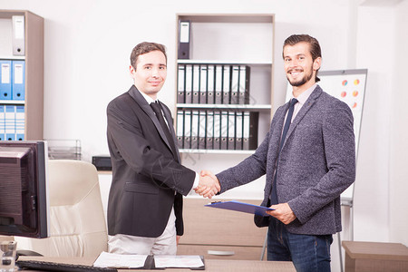 年轻的商业伙伴在办公室握手两个穿着正式西装的商人在公司办公图片