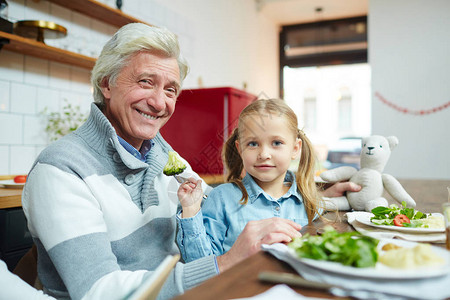小女孩在吃饭前用蒸的花椰菜喂外祖父时图片
