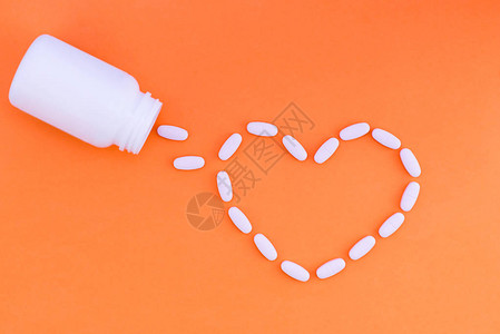 橙色背景上的药丸之心药片以心脏的形式从一个白色的药罐图片