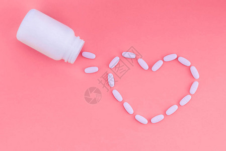 粉红色背景上的药丸之心药片以心脏的形式从一个白色的药罐图片