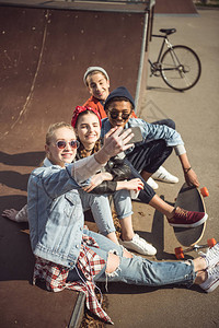 在滑板公园一起坐在一起时笑的青少年组背景图片
