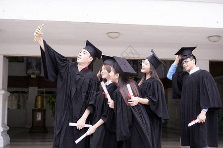一群成功的学生一起祝贺他们将毕业帽扔在空中并庆背景图片