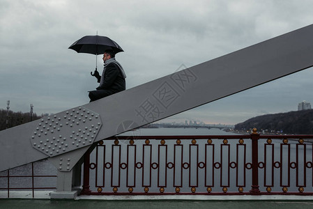 孤独的人撑着伞坐在桥上图片