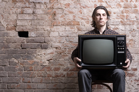 一个男人拿着复古电视机坐在背景图片