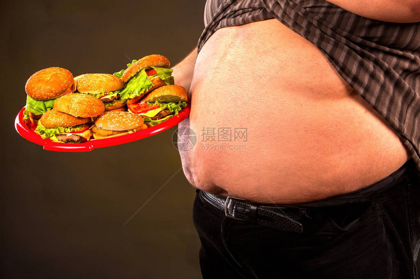 汉堡包组快餐的男人腹部脂肪超重者的早餐垃圾餐的裁剪镜头会导致肥胖人经常在黑色背图片