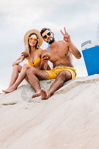 一对年轻夫妇的底部景色椰子鸡尾酒坐在云天前沙地上图片