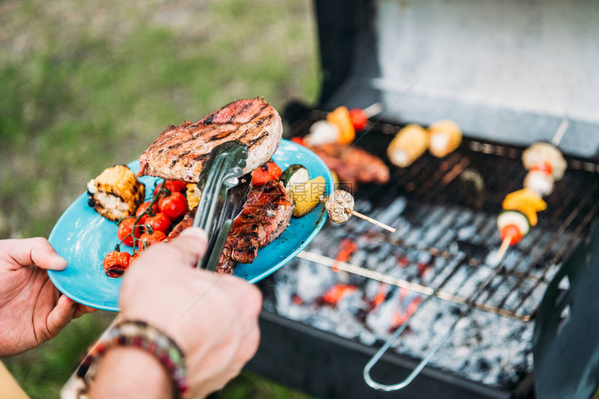 在公园的bbq时将烤食物放在盘子上图片