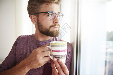 有思想的男人端着咖啡望着窗外背景图片