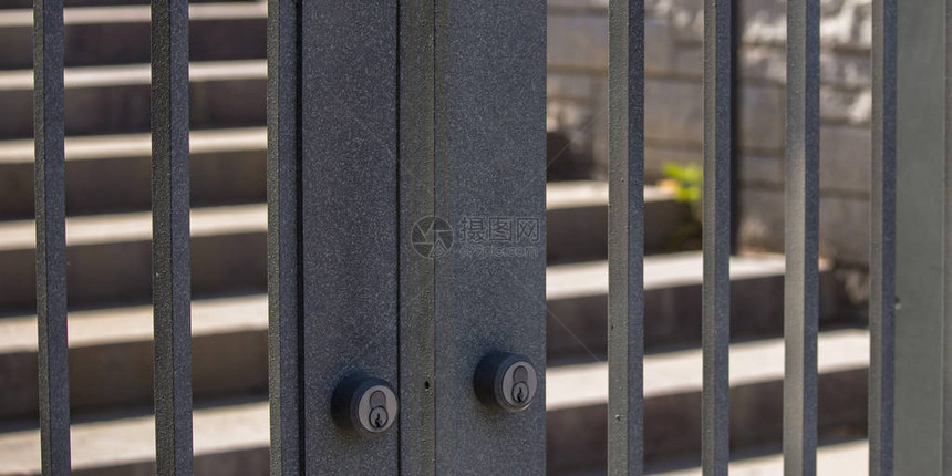 带钥匙孔的门通向阳光明媚的楼梯带有两个钥匙孔的灰色双门的特写镜头带有水平金属条的大门通向被阳光照亮的宽阔图片