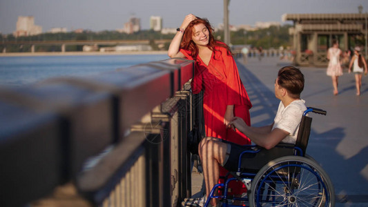 穿着红头发的女孩和穿轮椅的男女孩在夏夜在海滨聊天图片