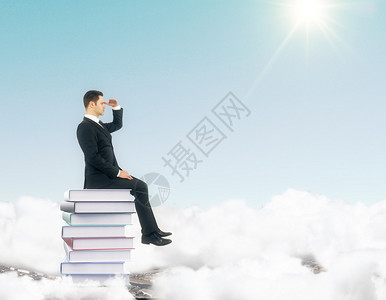 商人坐在云顶的一堆书上看着远处图片