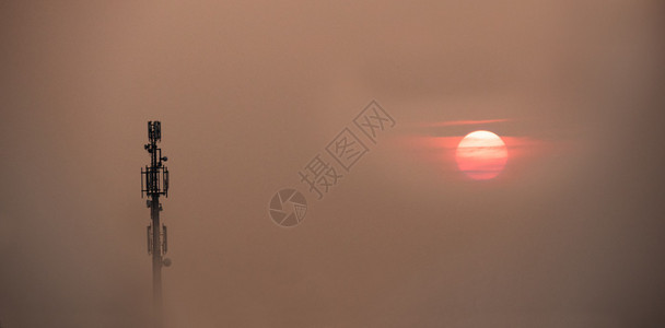 手机天线塔从雾中出现在夕阳的天空胶片颗粒效果概念背景图片