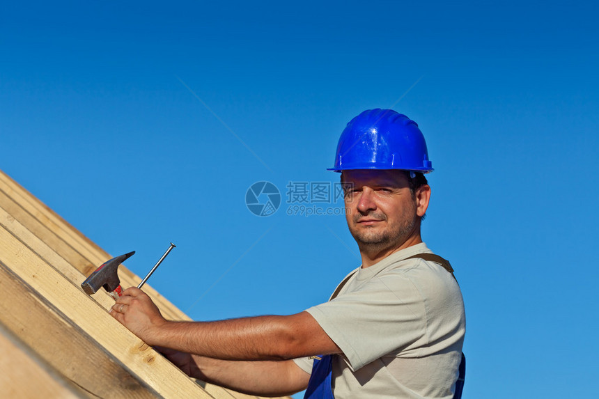 以铁钉和锤子在屋顶结构上建房的图片