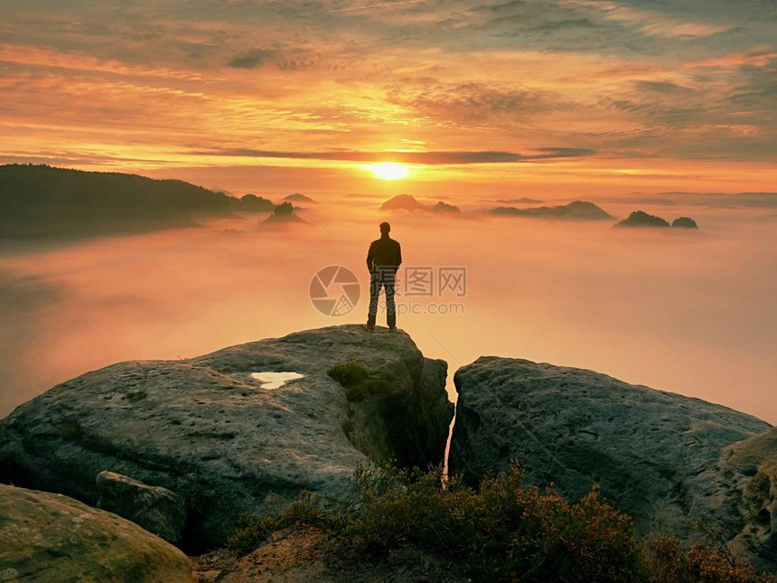 人独自站在岩石的顶端徒步旅行者在地平线上观看秋天的太阳美丽的时刻图片