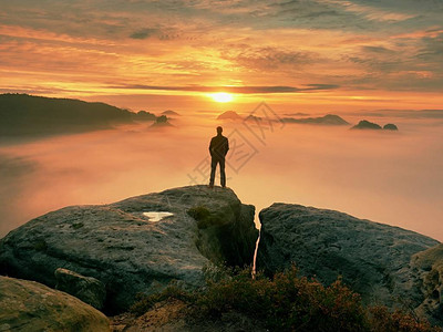 人独自站在岩石的顶端徒步旅行者在地平线上观看秋天的太阳美丽的时刻背景图片