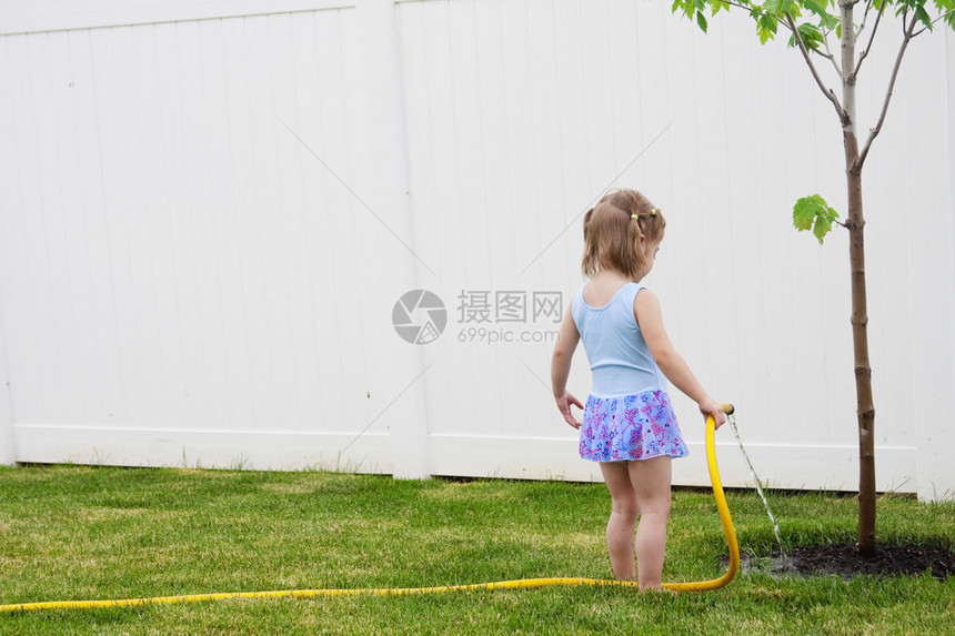 年轻女孩在后院里浇灌一棵小树图片