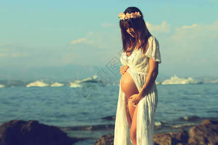 身着白色洋装的美丽的孕妇在海图片