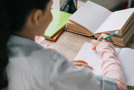 小学生坐在办公桌前做作业时在笔记本上写字的背影图片