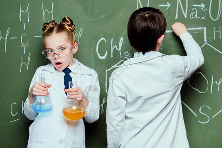 穿白大褂的男孩和女孩站在烧瓶里的试剂和在科学实验室图片