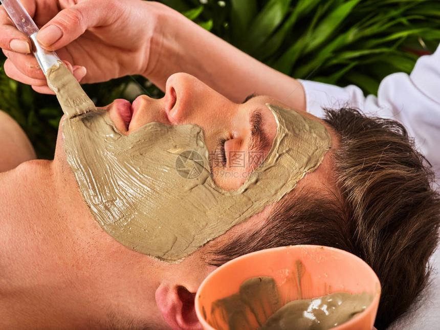 人在温泉沙龙的泥面膜用粘土全脸按摩与治疗室的女孩男人躺在木制温泉床上背景中的绿色棕榈叶图片