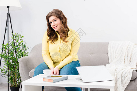 坐在沙发上与笔记本电脑坐在咖啡桌上的青年妇女肖像图片