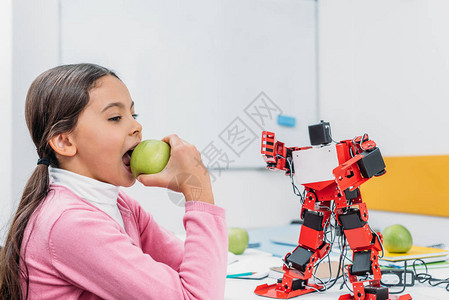 女孩在STEM课堂上吃苹果和与机器人模型图片