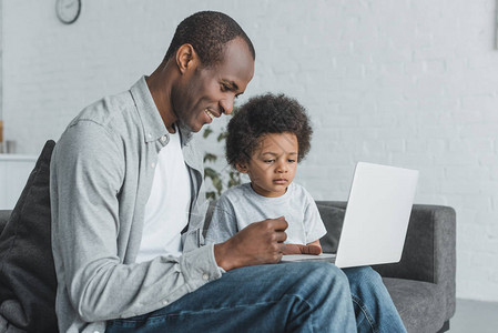 在笔记本电脑上和儿子一起在家看东西的非洲美国父图片