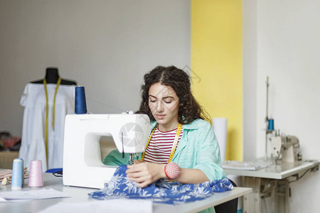 在现代缝纫车间使用缝纫机与织物一起工作的彩色衬衫和条纹T恤图片