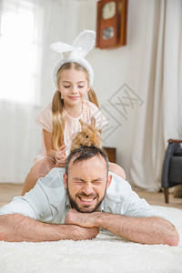 父亲和女儿在家里玩兔子在白毛地毯图片