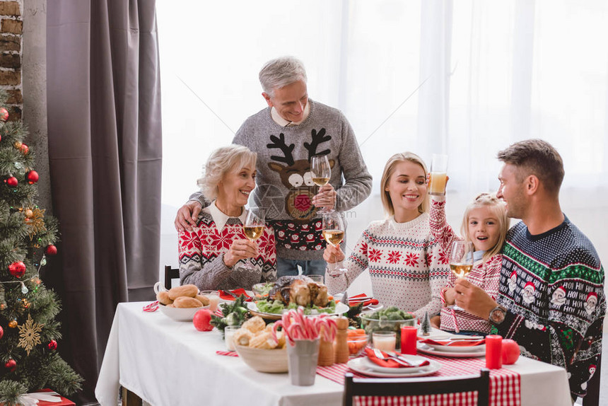 家庭成员坐在桌边在圣诞节拿着红酒杯图片