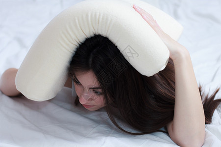 睡不着的年轻女子用枕头盖住头白种女人背景图片
