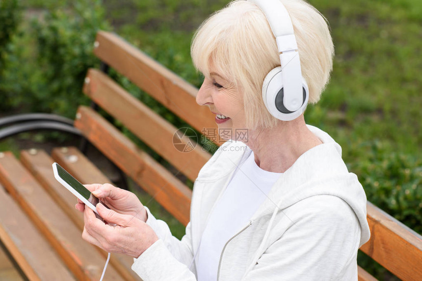 笑着微笑的老年妇女用耳机和智能图片