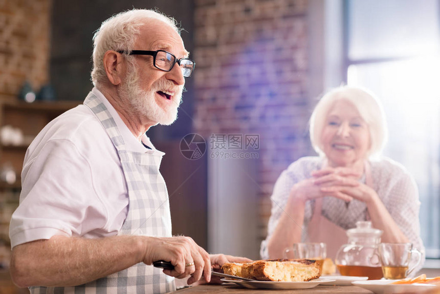 老人与附近的妻子切自制馅饼的侧面图图片