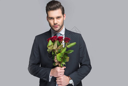 高雅的男子拿着红玫瑰花束在灰图片
