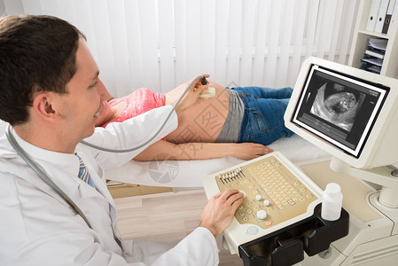 快乐的男医生移动超声波播放器在孕妇眼看图片