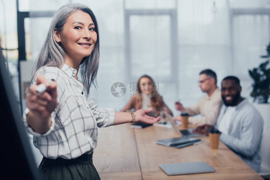 微笑的亚洲女商人用记号笔和她的多元文化同事指着背景图片