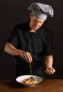 在黑色背景上准备食物的厨师图片