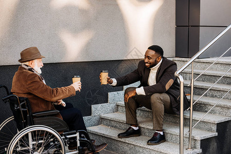 坐在轮椅上快乐的老年残疾人和非洲裔美国人一起喝咖啡图片