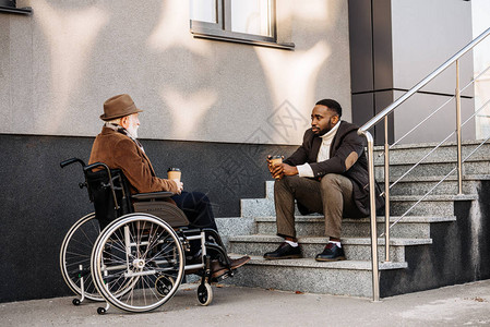 坐在轮椅和非洲裔美国康乐的老年残疾人一起喝咖啡图片