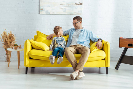 快乐的父亲和儿子坐在黄色沙发图片